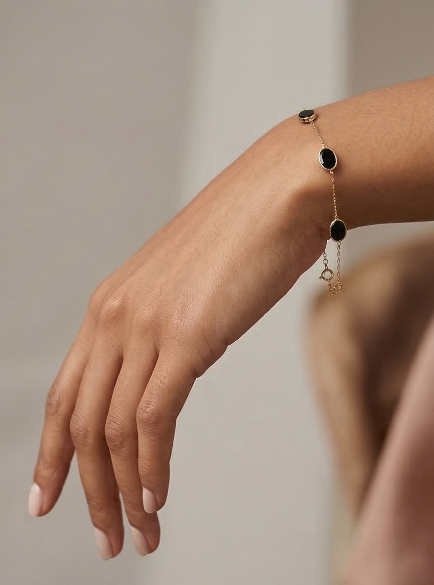 Close-up of a hand wearing a delicate bracelet with onyx black enamel on a neutral background